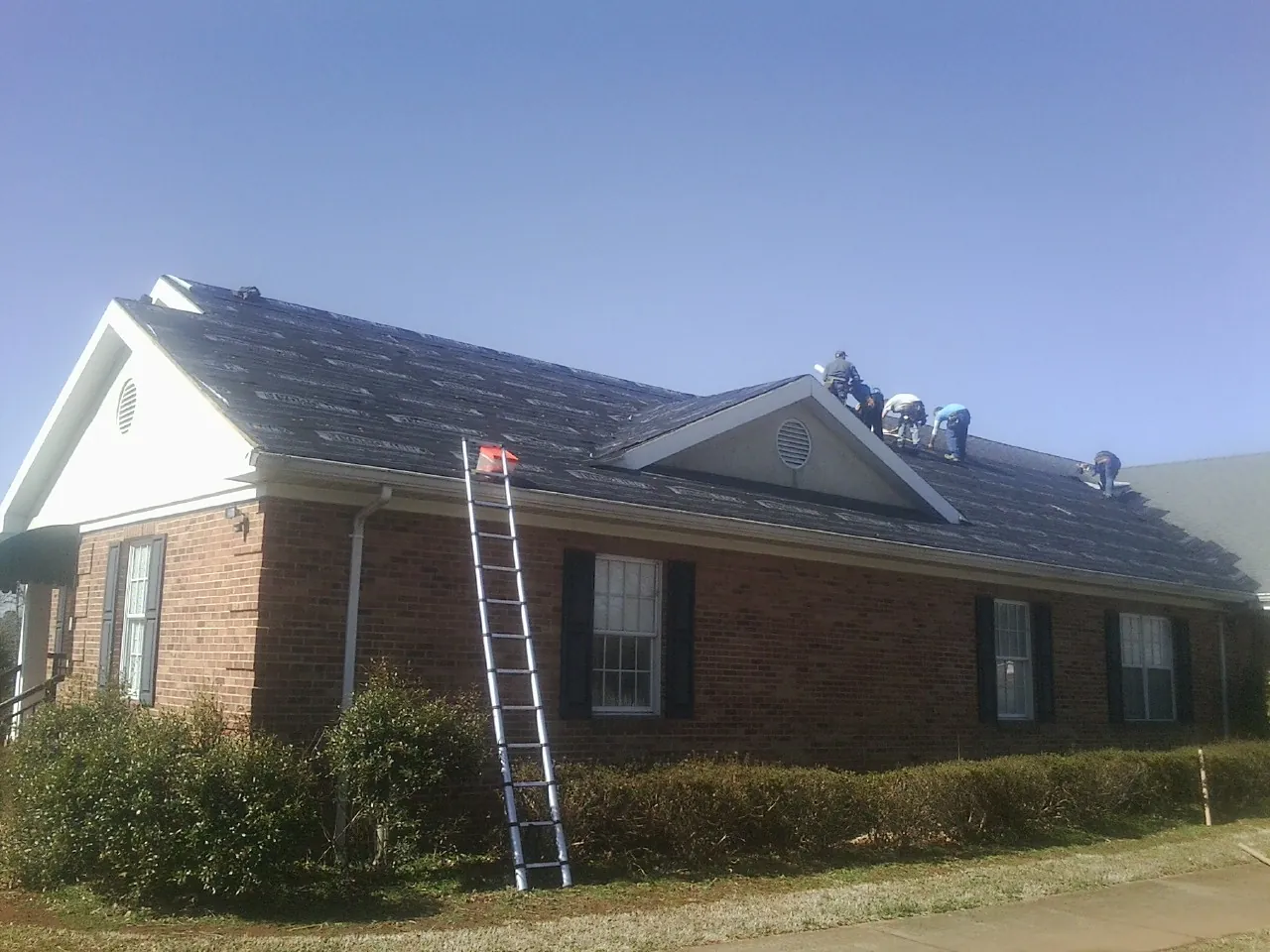 Crew tearing shingles off a brick ranch roof with a ladder set — Metal Roof Repair work by our crew in Bloomsburg