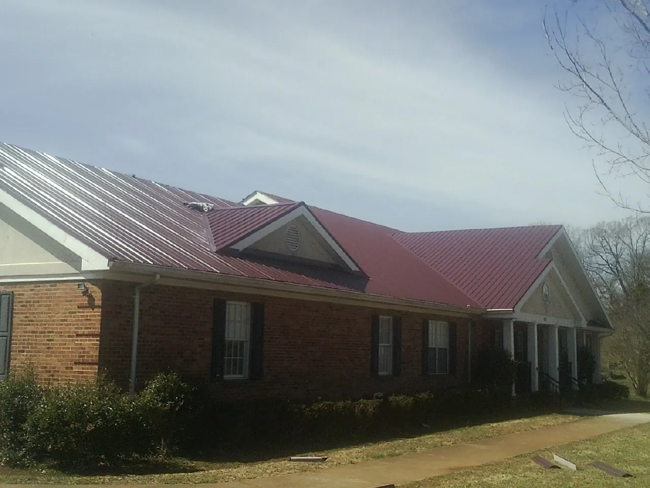 Red metal roof with gabled entries on a long brick building, from a Hail Damage Roof Repair job in Bloomsburg