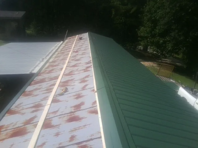 Old rusted panels beside newly installed green metal roofing — Wind Damage Roof Repair by Roofing Brothers in Bloomsburg