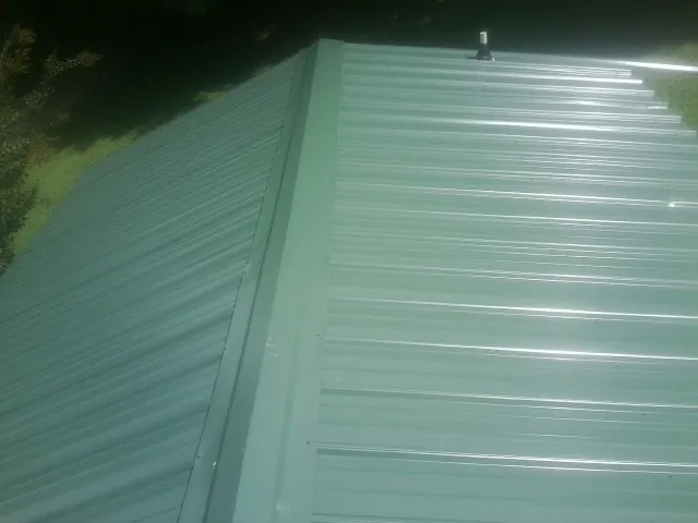 New green metal panels meeting at the ridge of a roof — Flat Roof Repair work by our crew in Bloomsburg