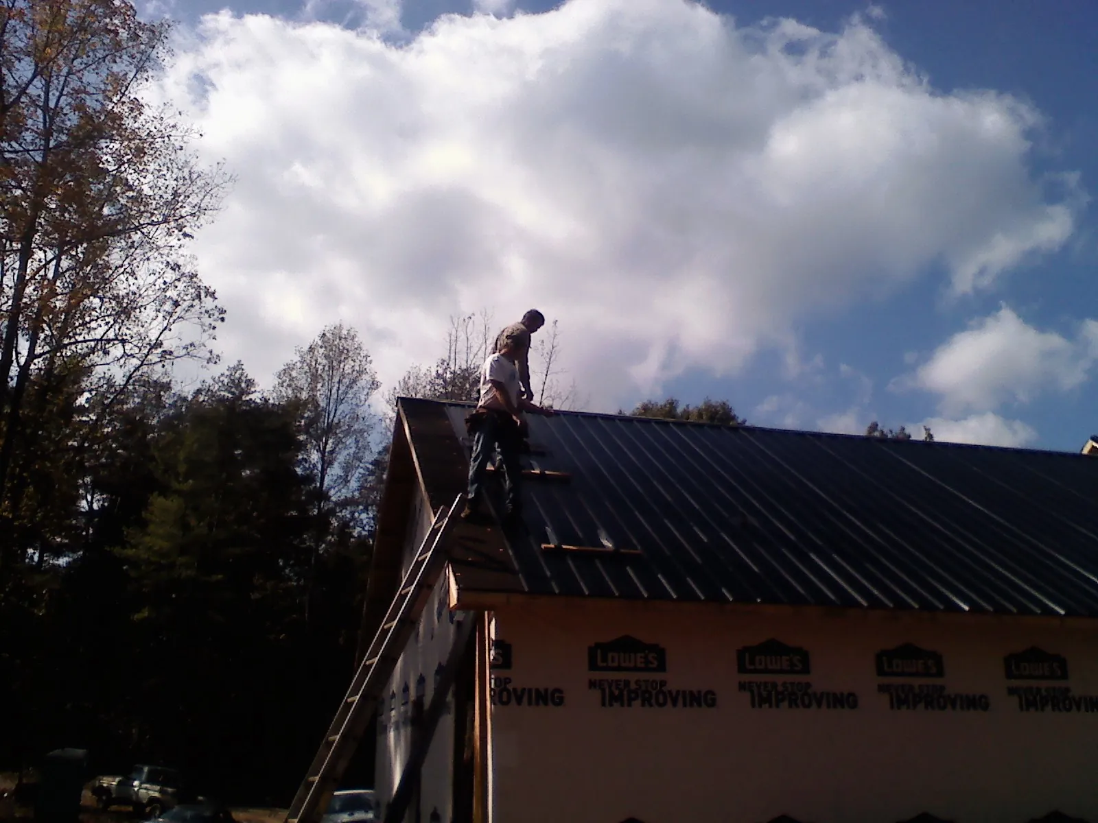 Roofer fastening dark metal panels high against a cloudy sky, from a Roof Inspection job in Bloomsburg