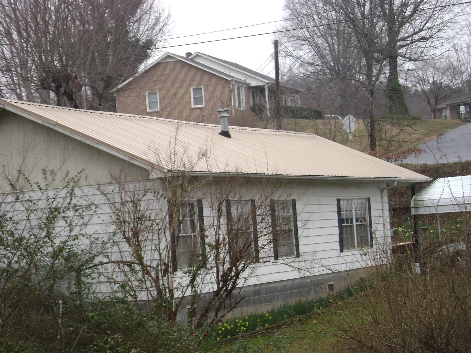 Tan metal roof on a white sided house set into a hillside — Commercial Roofing by Roofing Brothers in Bloomsburg